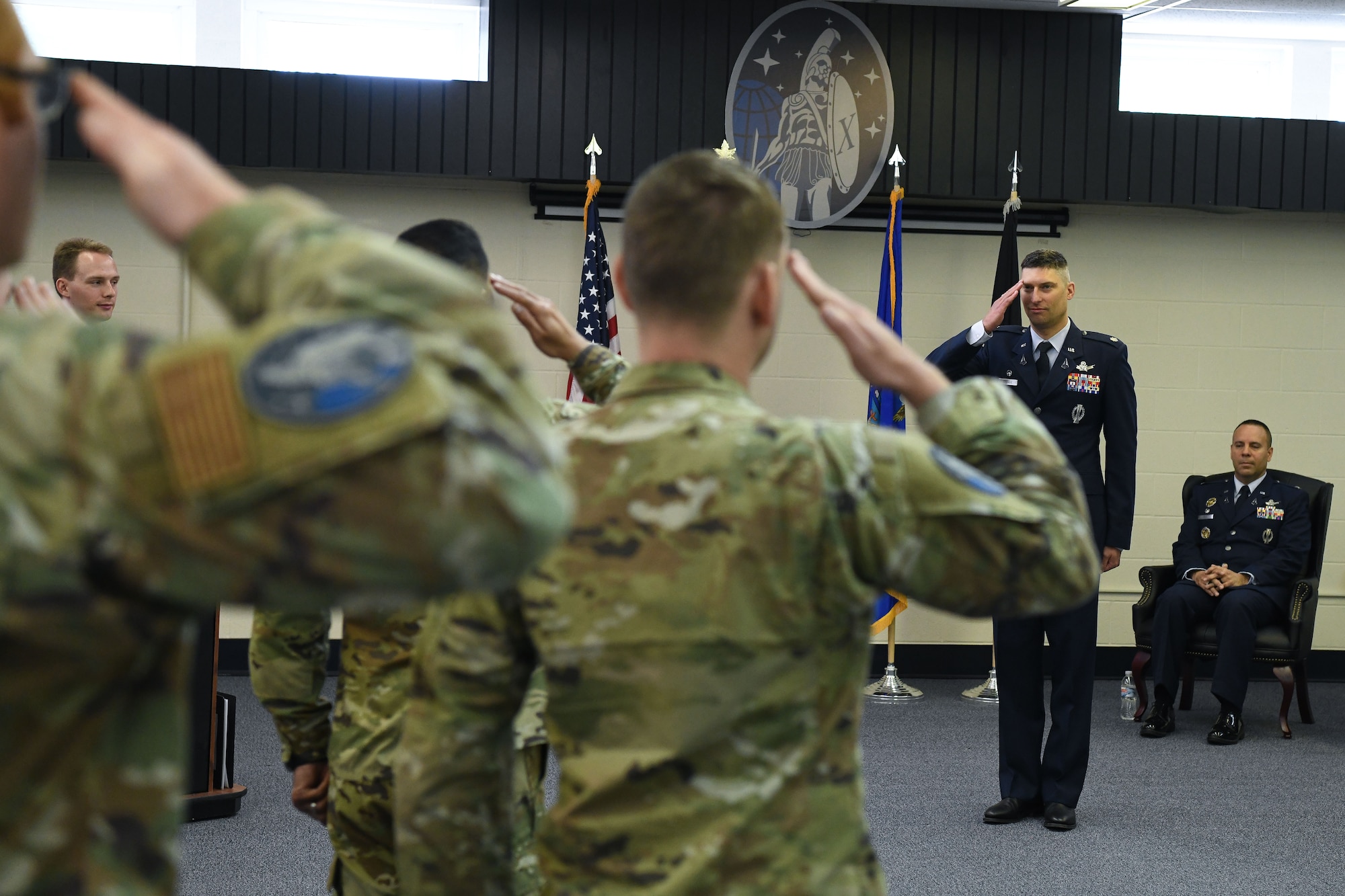 Man in blue suit salutes military members.