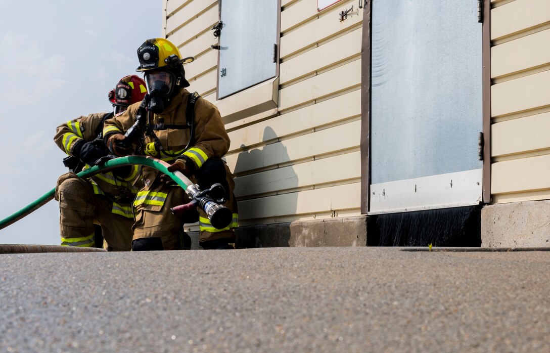 Mr. Wayne Kolve (left), 28th Civil Engineer Squadron fireman, and U.S. Air Force Airman 1st Class Matthew Frankle, 28th CES fireman, stand by in case of an emergency during a structural fire exercise at Ellsworth Air Force Base, South Dakota, June 13, 2023.