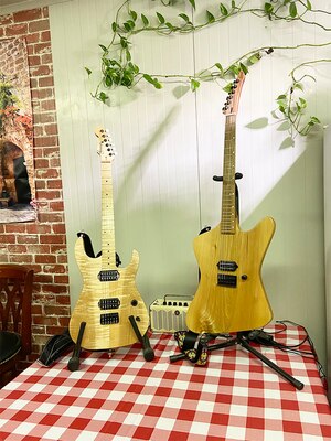 Two custom guitars sit on a table with checkered tablecloth.