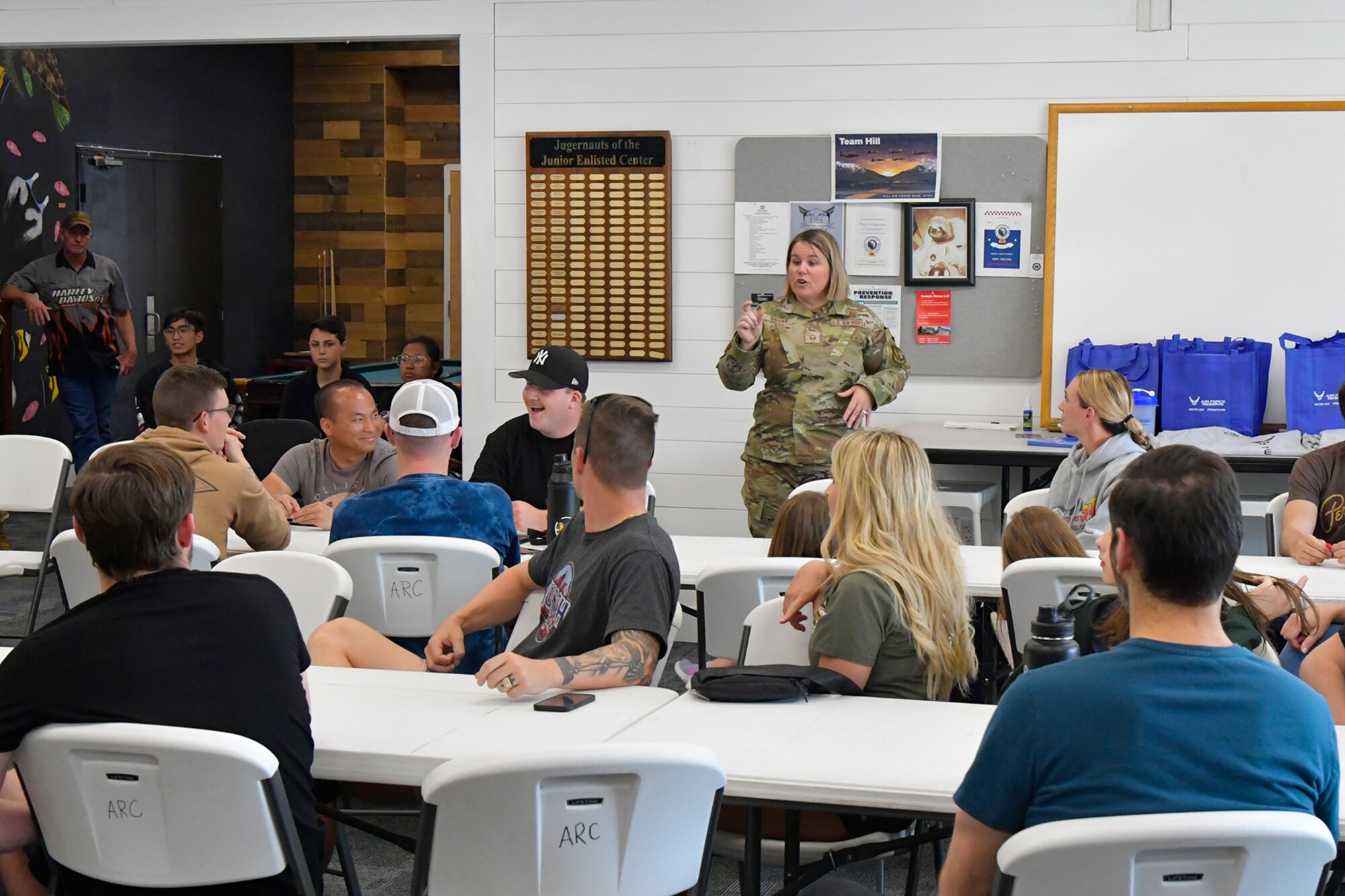 A military member leads a group of people who are seated around tables