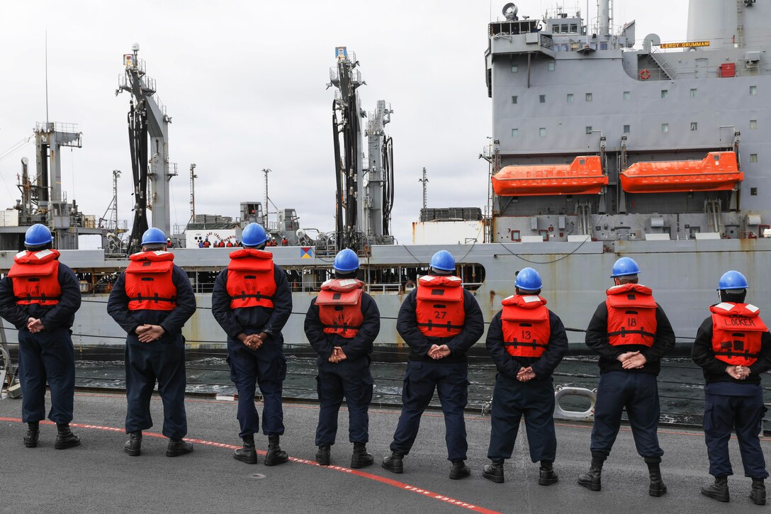 Sailors stand side by side at parade rest during a replenishment at sea.