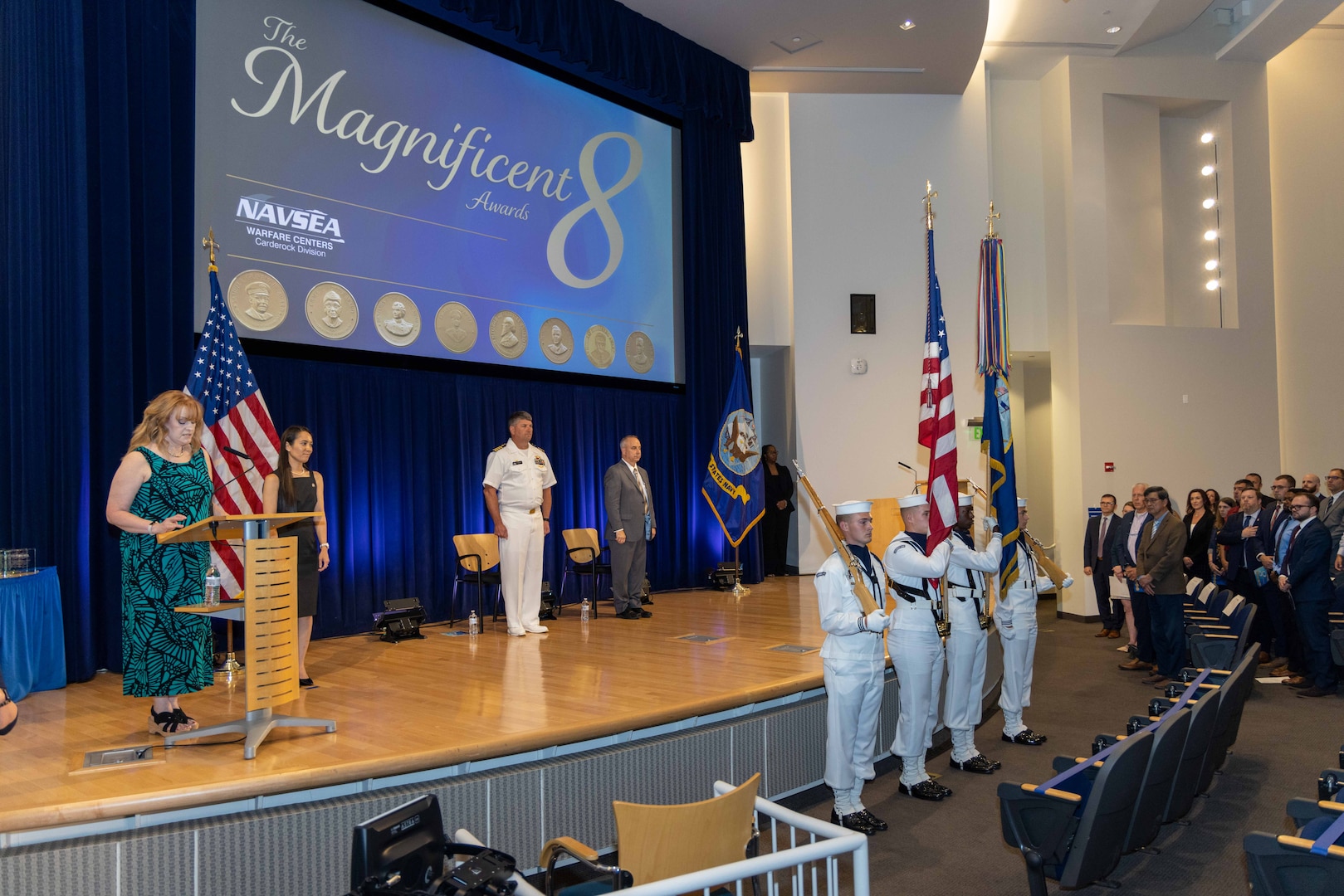 Naval Surface Warfare Center, Carderock Division administrative specialist Sue Rossi (left) introduces engineer Sharon Collins (second to left) to perform the National Anthem during the Magnificent Eight Award ceremony in West Bethesda, Md., on June 13. Carderock's Commanding Officer Capt. Matthew Tardy (third from left) and Technical Director Larry Tarasek (fourth from left) stand at attention as the Color Guard posts colors. (U.S. Navy photo by Aaron Thomas)