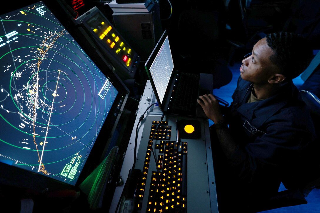A sailor looks up at computer monitors.