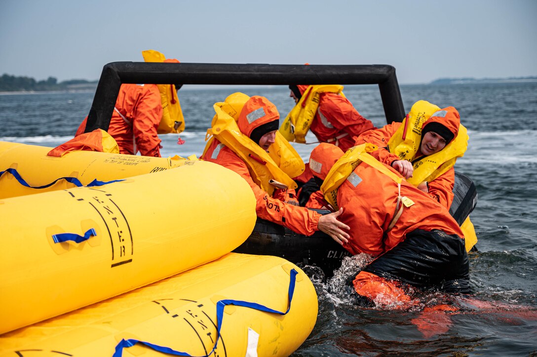 Airmen work to pull another service member into a raft.