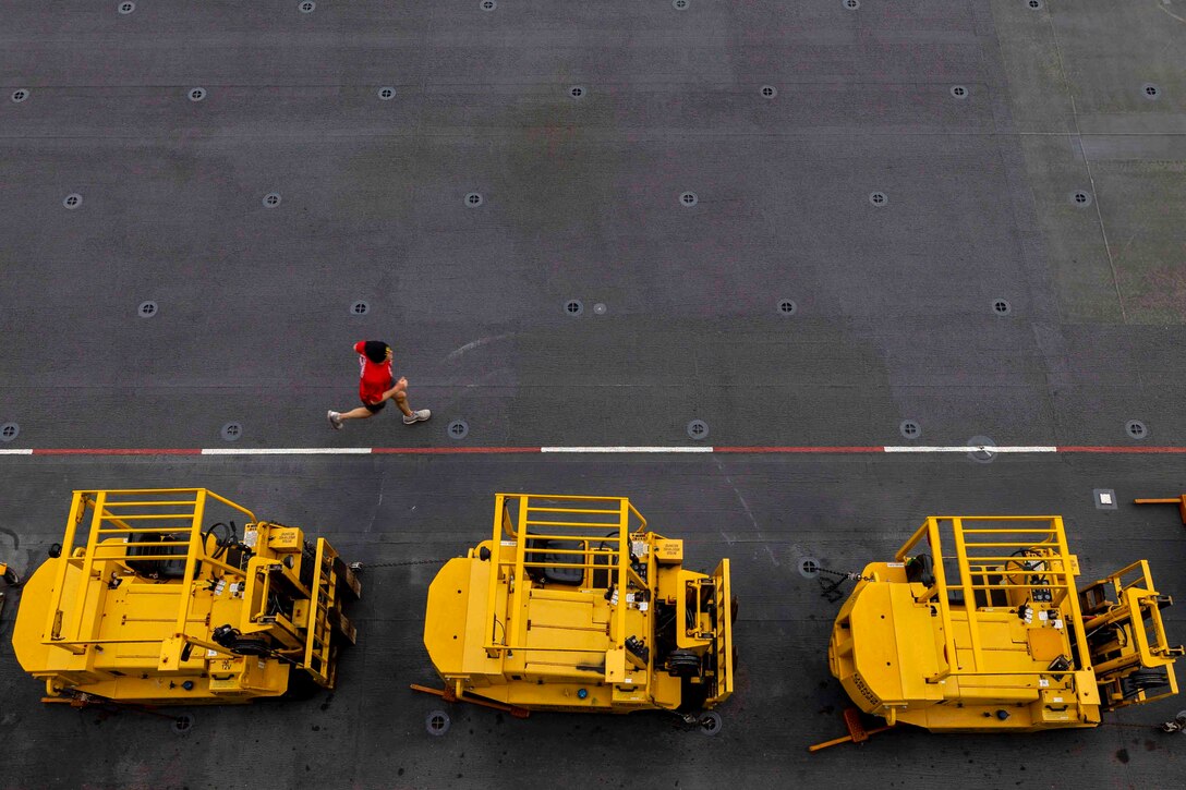 A sailor runs next to three military equipment vehicles.