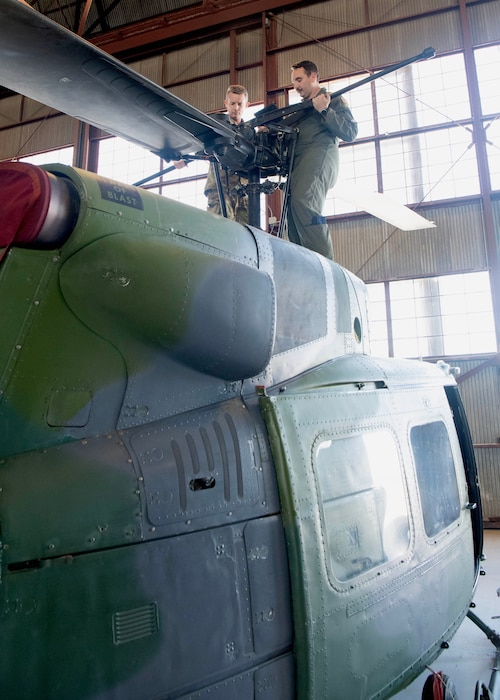 Two men on top of helicopter, performing maintenance on the rotary blades.