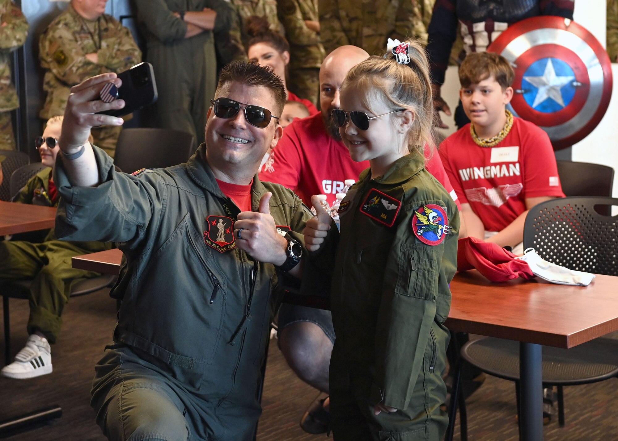 Air Force pilot in green flight suit and sunglasses takes a selfie with a little girl in green flight suit