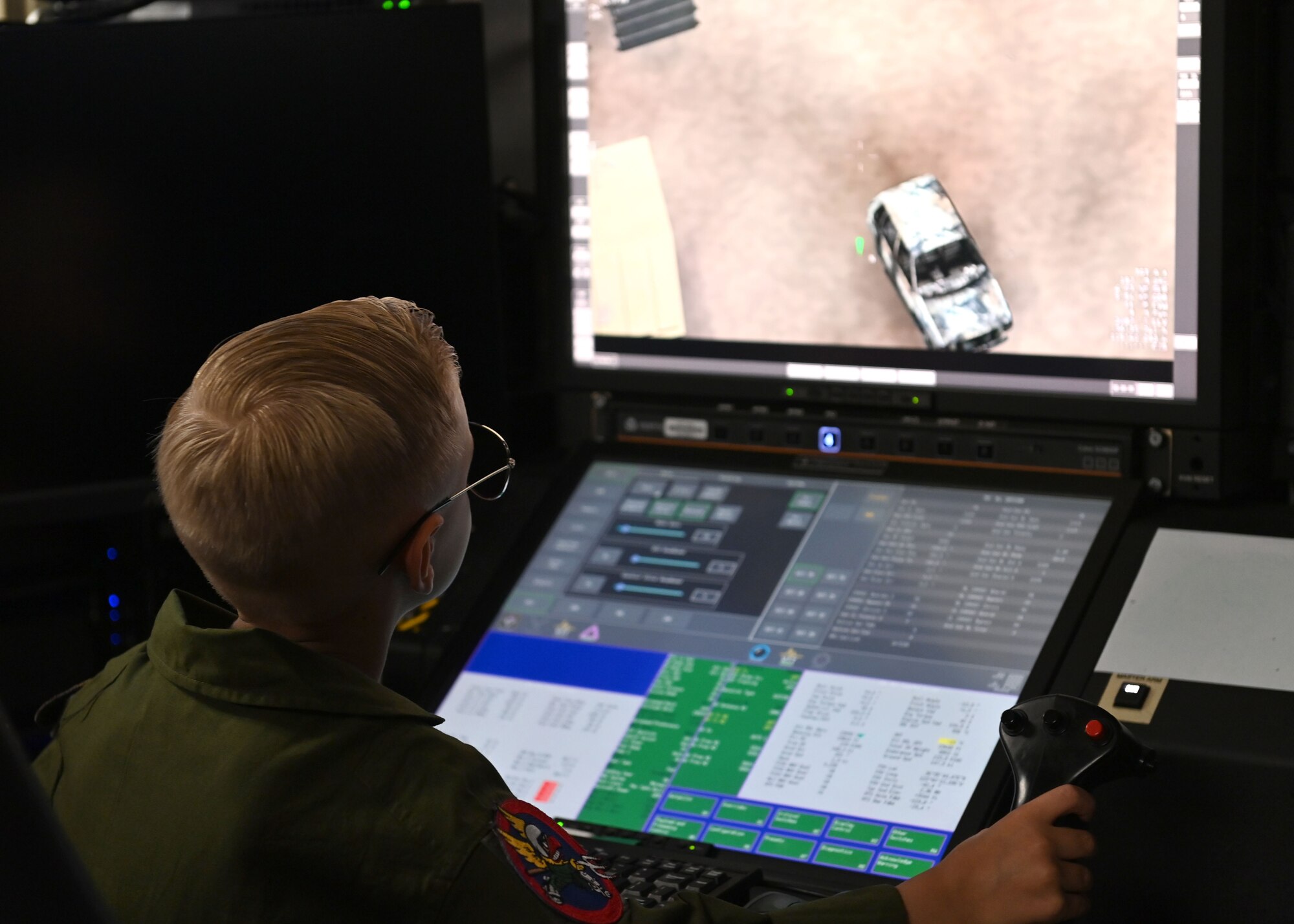 Blonde boy with glasses wearing green flight suit operates a flight simulator