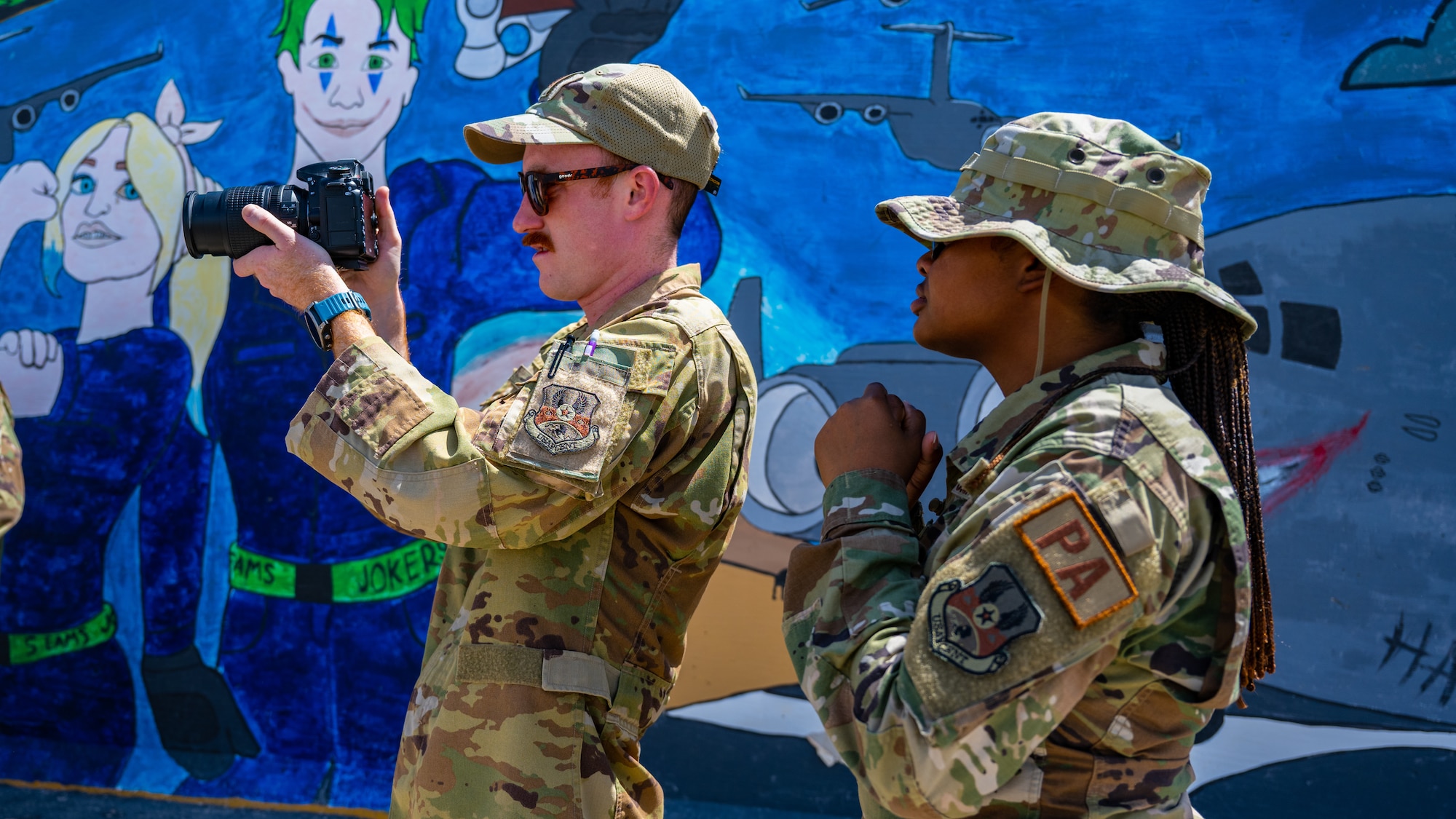 U.S. Air Force Staff Sgt. Breanna Diaz, 386th Air Expeditionary Wing public affairs specialist (right), coaches an Airman from the 386th AEW safety office during alert photography training at Ali Al Salem Air Base, Kuwait, June 21, 2023. The 386th AEW safety team attended the training to learn what goes into alert photography, and how it assists with a variety of scenarios and investigations.