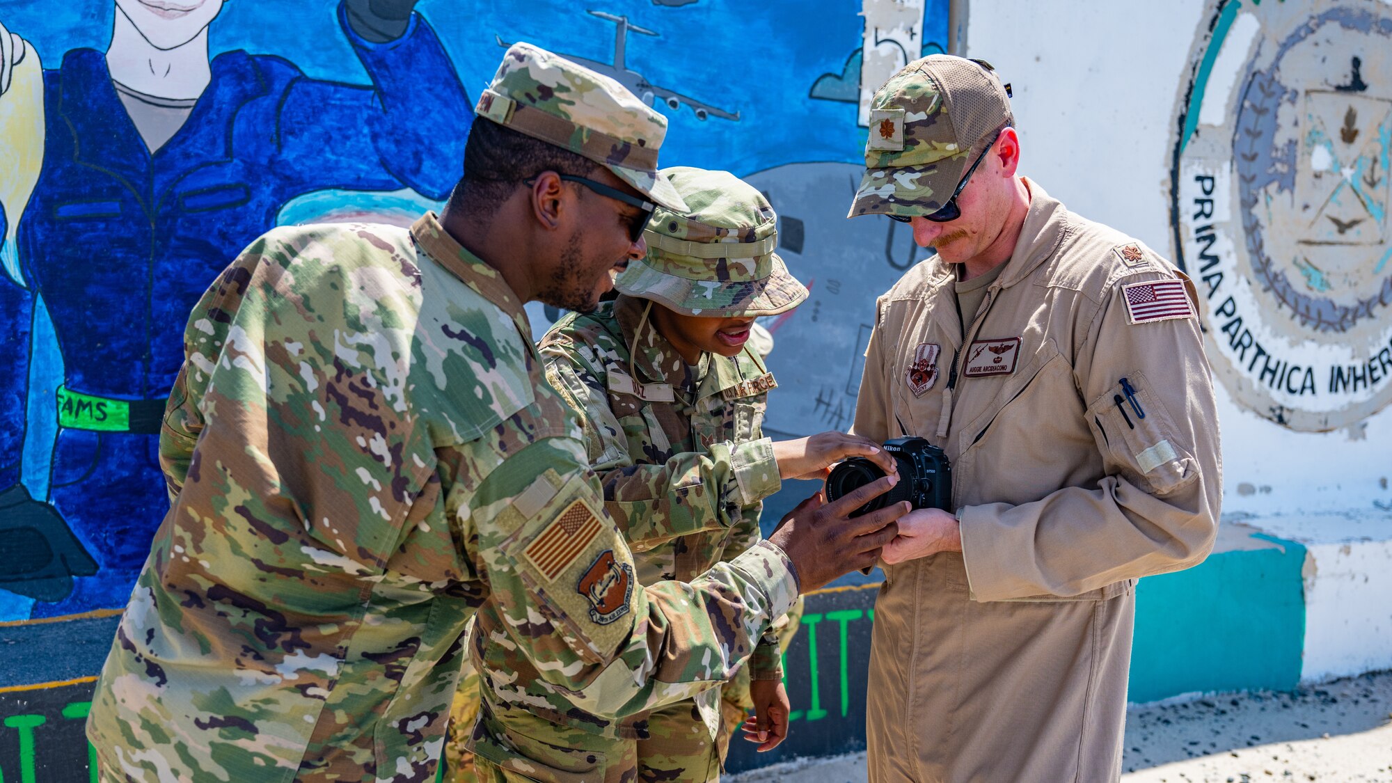 U.S. Air Force Tech. Sgt. Isaac Garden, 386th Air Expeditionary Wing NCOIC of command information (left), and Staff Sgt. Breanna Diaz, 386th AEW public affairs specialist (middle), teach camera operations to an Airman from the 386th AEW safety office during alert photography training at Ali Al Salem Air Base, Kuwait, June 21, 2023. The 386th AEW safety team attended the training to learn what goes into alert photography, and how it assists with a variety of scenarios and investigations.