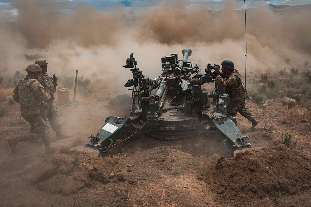 Soldiers fire a howitzer creating large clouds of dust and dirt.