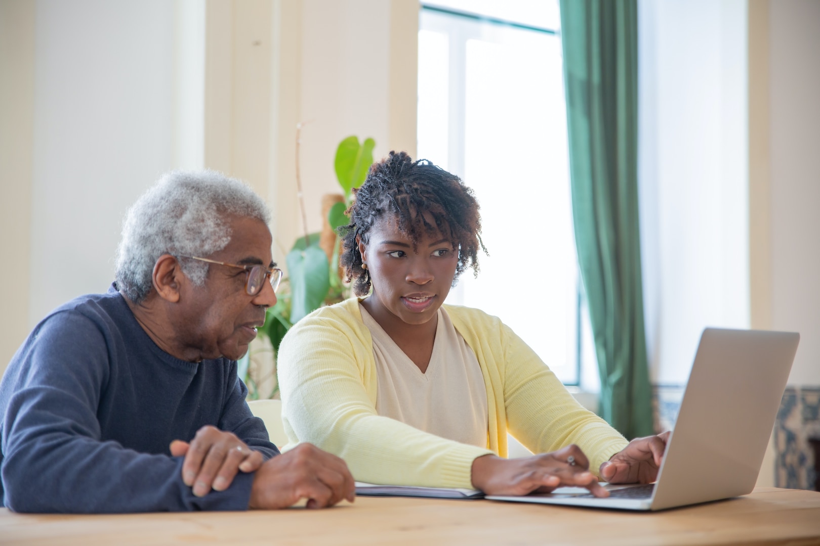 Young person helping older man use laptop