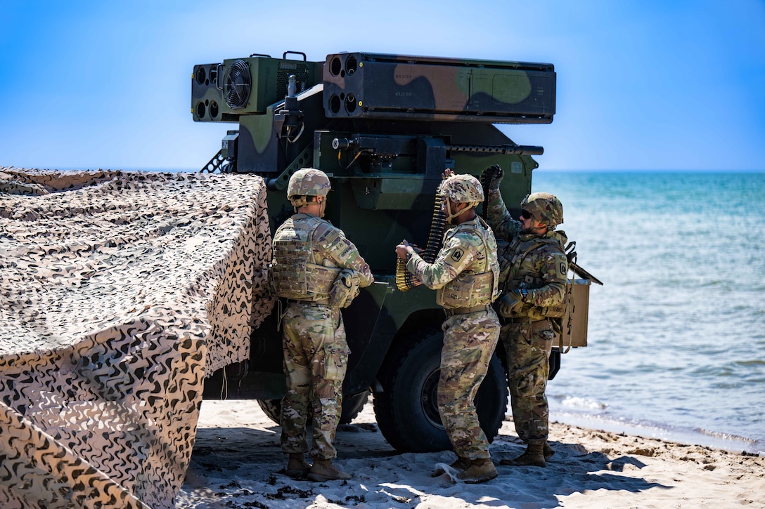 Soldiers prepare to load a large weapon on a beach.