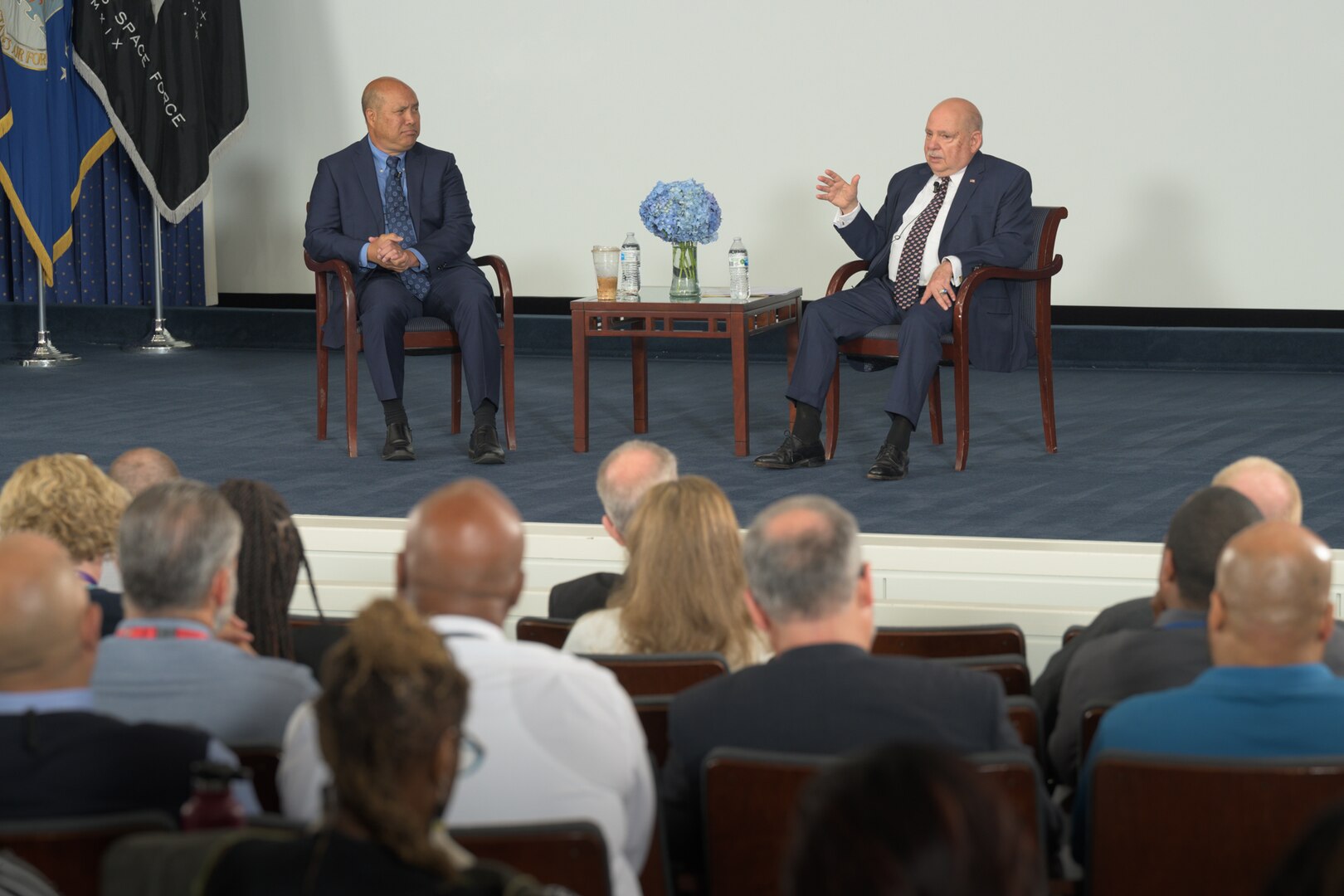 two men sitting on a stage talking to an audience