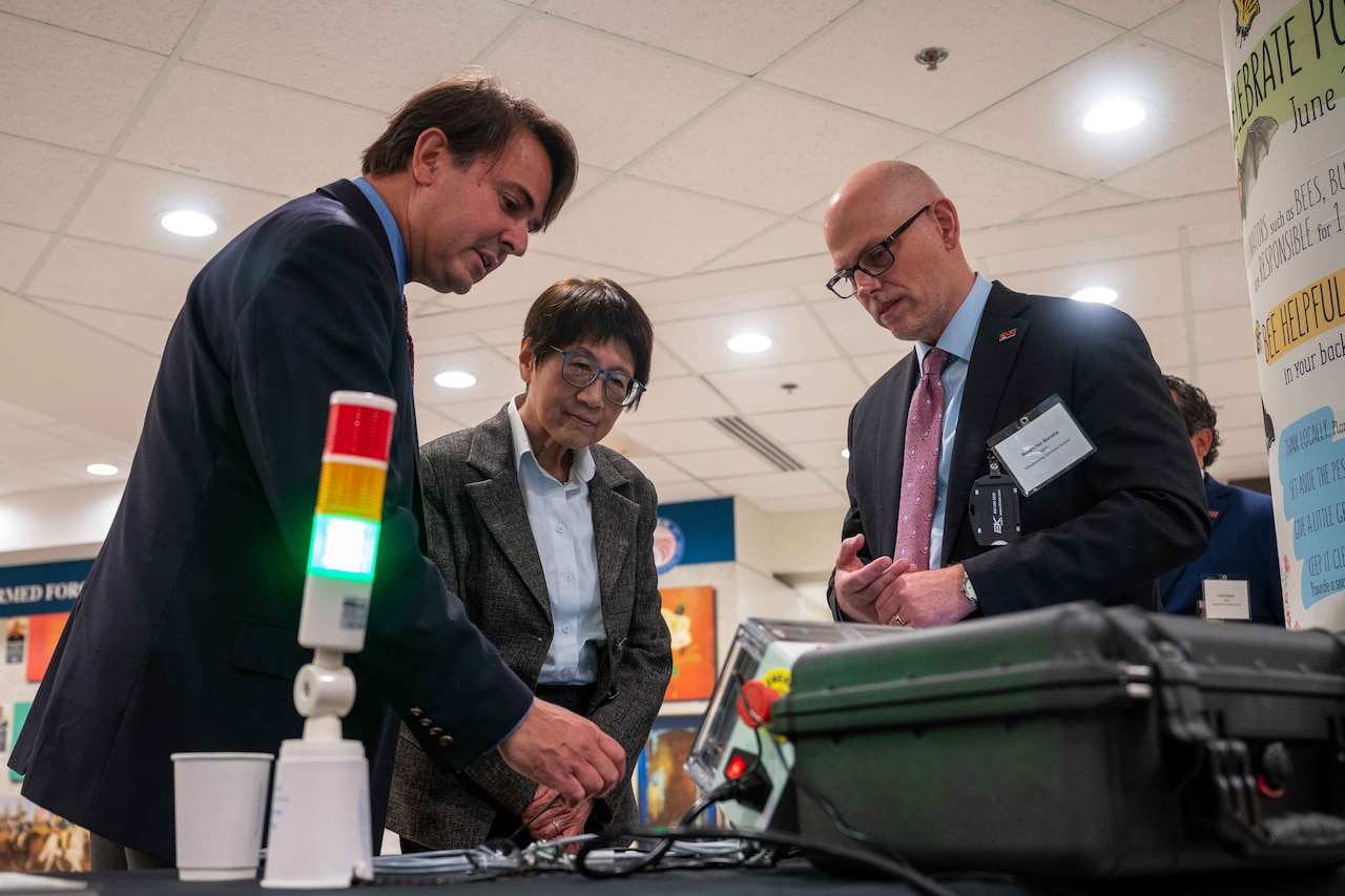 Three people look at a table displaying tech products.