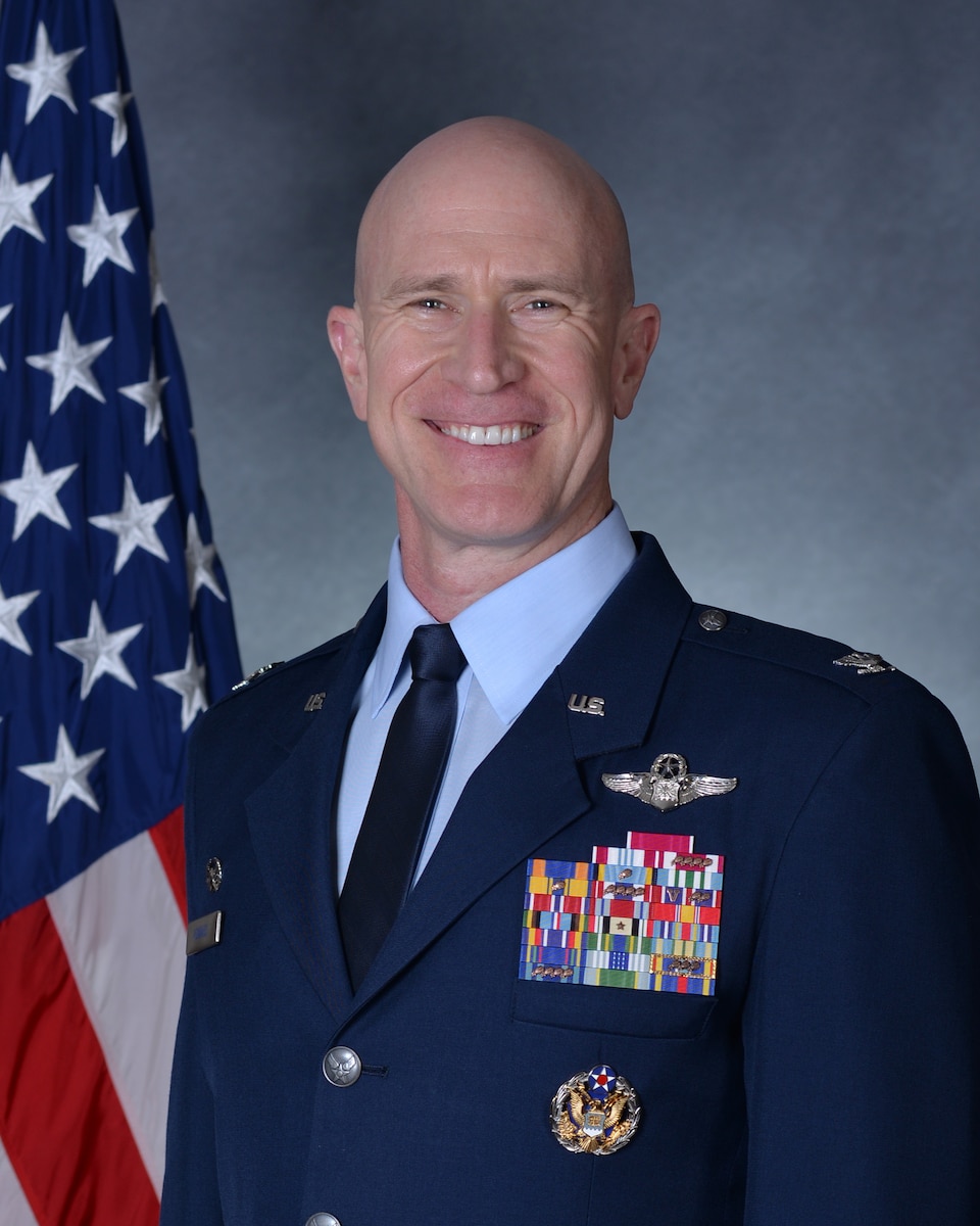 Man in dress blues posing for official photo in front of U.S. flag