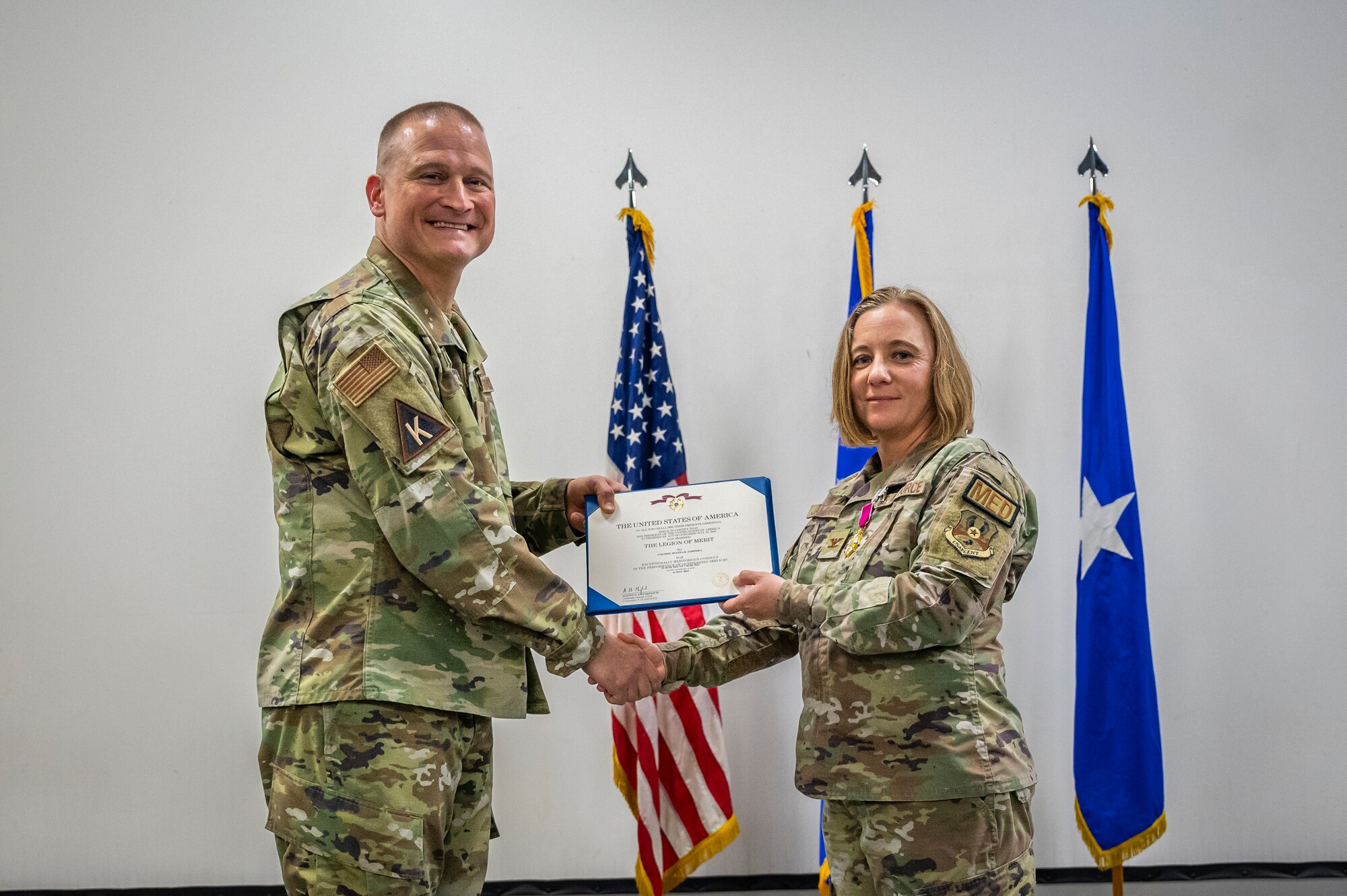 Military members in uniform pose for a photo while passing a certificate to each other.