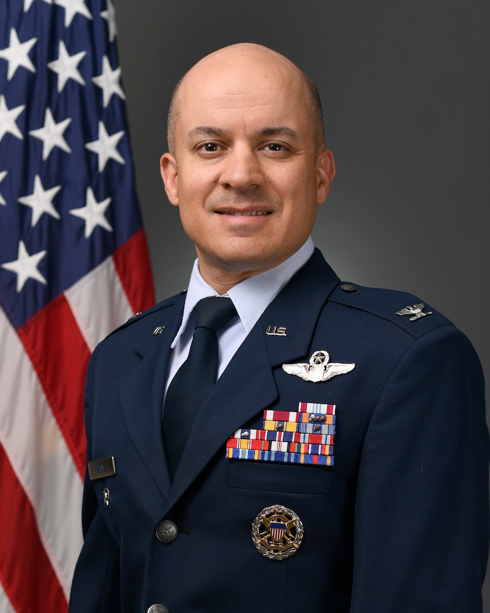 Man in dress blues uniform in front of U.S. flag