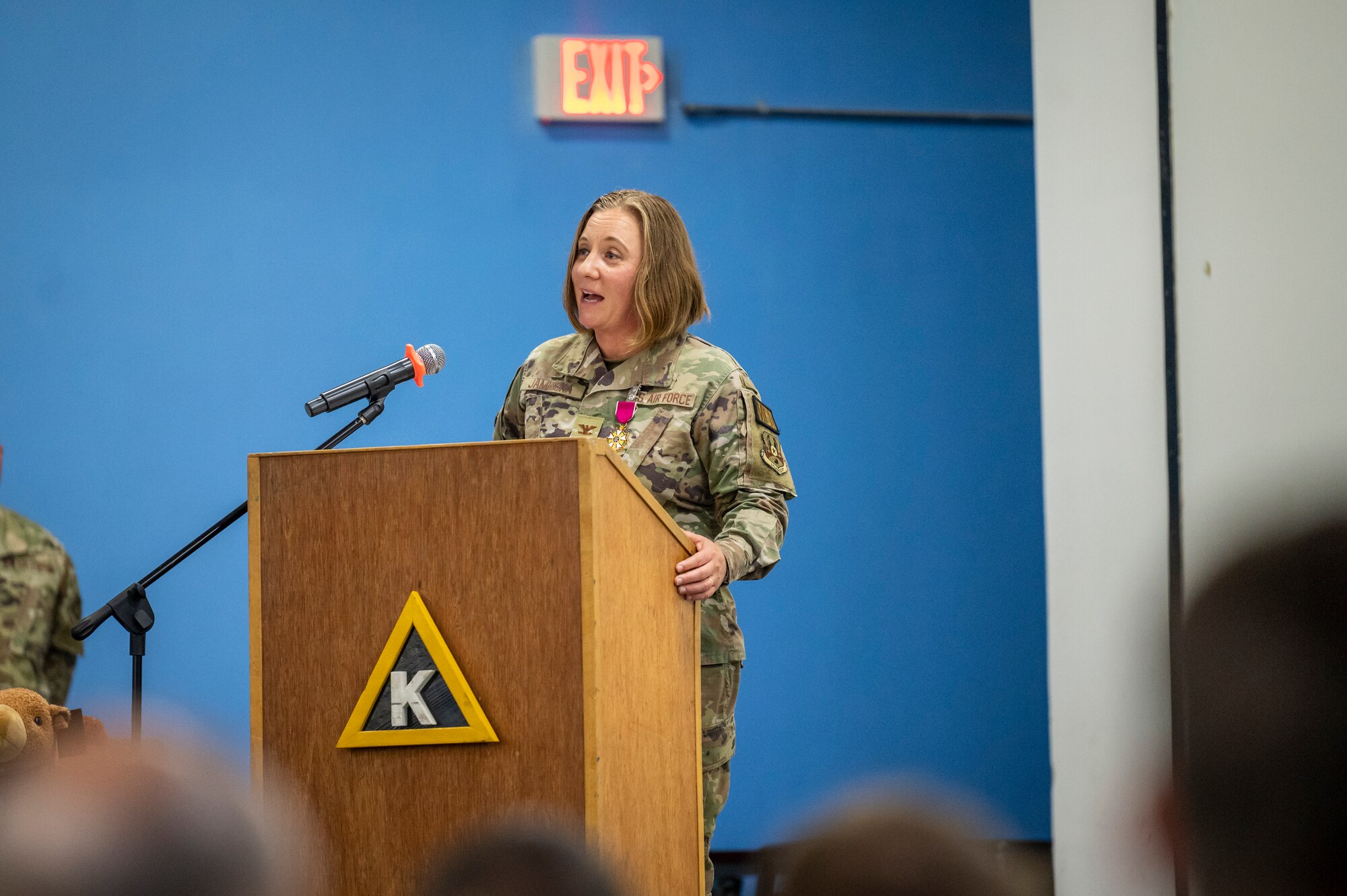 Military member in uniform stands at a podium on stage and gives a speech to the crowd