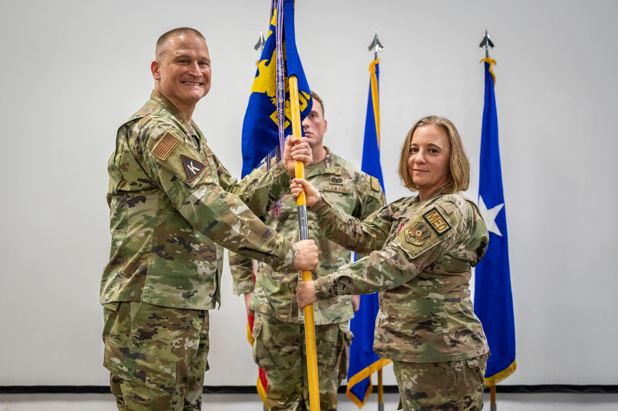 Military members in uniform pose for a photo while passing a flag pole to each other.