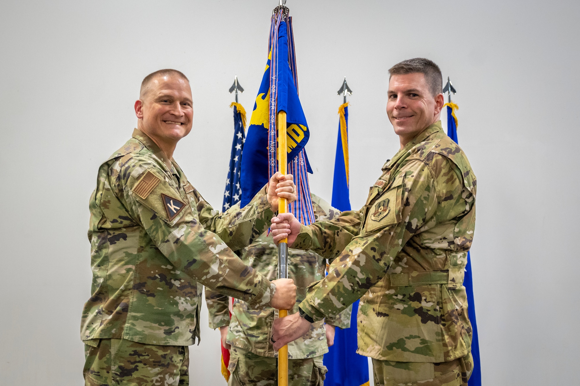 Military members in uniform pose for a photo while passing a flag pole to each other.