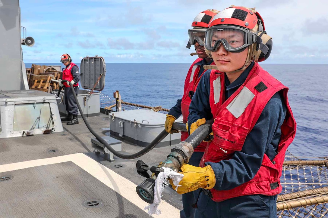 Sailors hold a fire hose on the flight deck of a Navy ship.