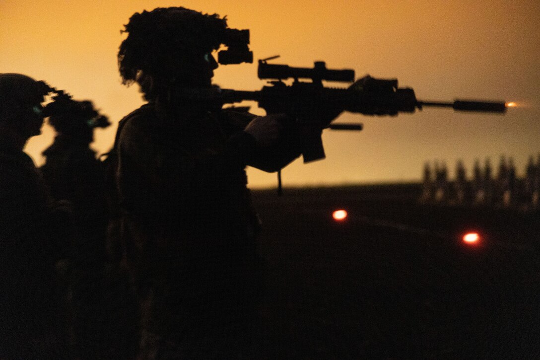 Marines are shown in silhouette, firing weapons.