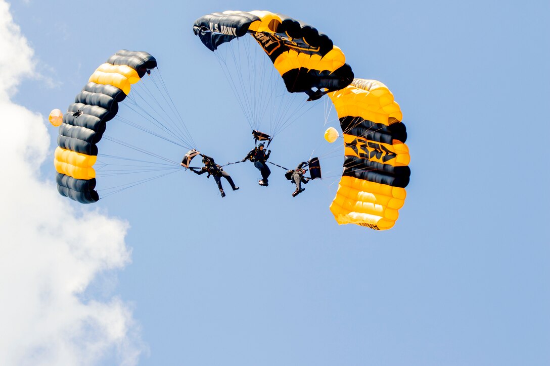 Three parachutists perform in the air with a cloud on their left.