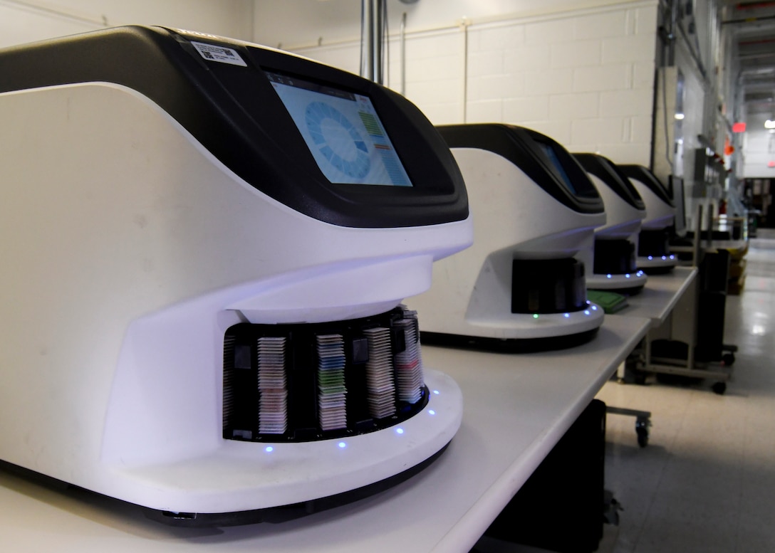 Four short white machines, each about the size of a microwave, sit on a table in a dimly lit room.