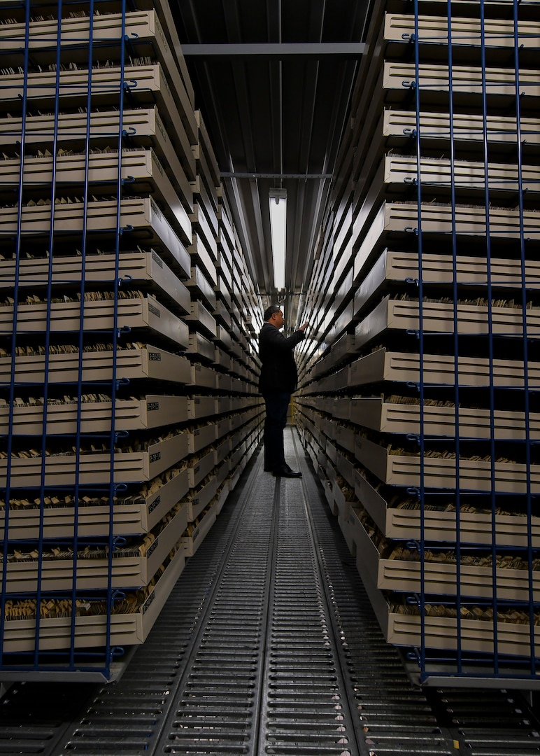 A man stands between two rows of trays. Each row is taller than the man standing in the photo.