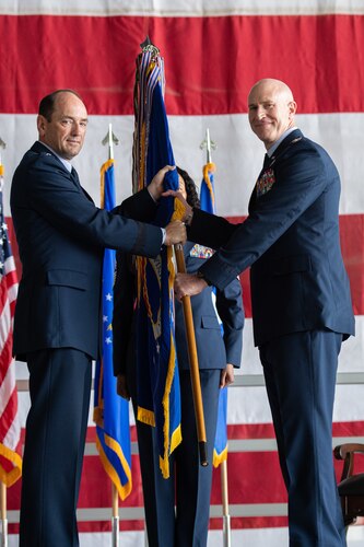 Uniformed man hands blue and yellow guidon to another uniformed man