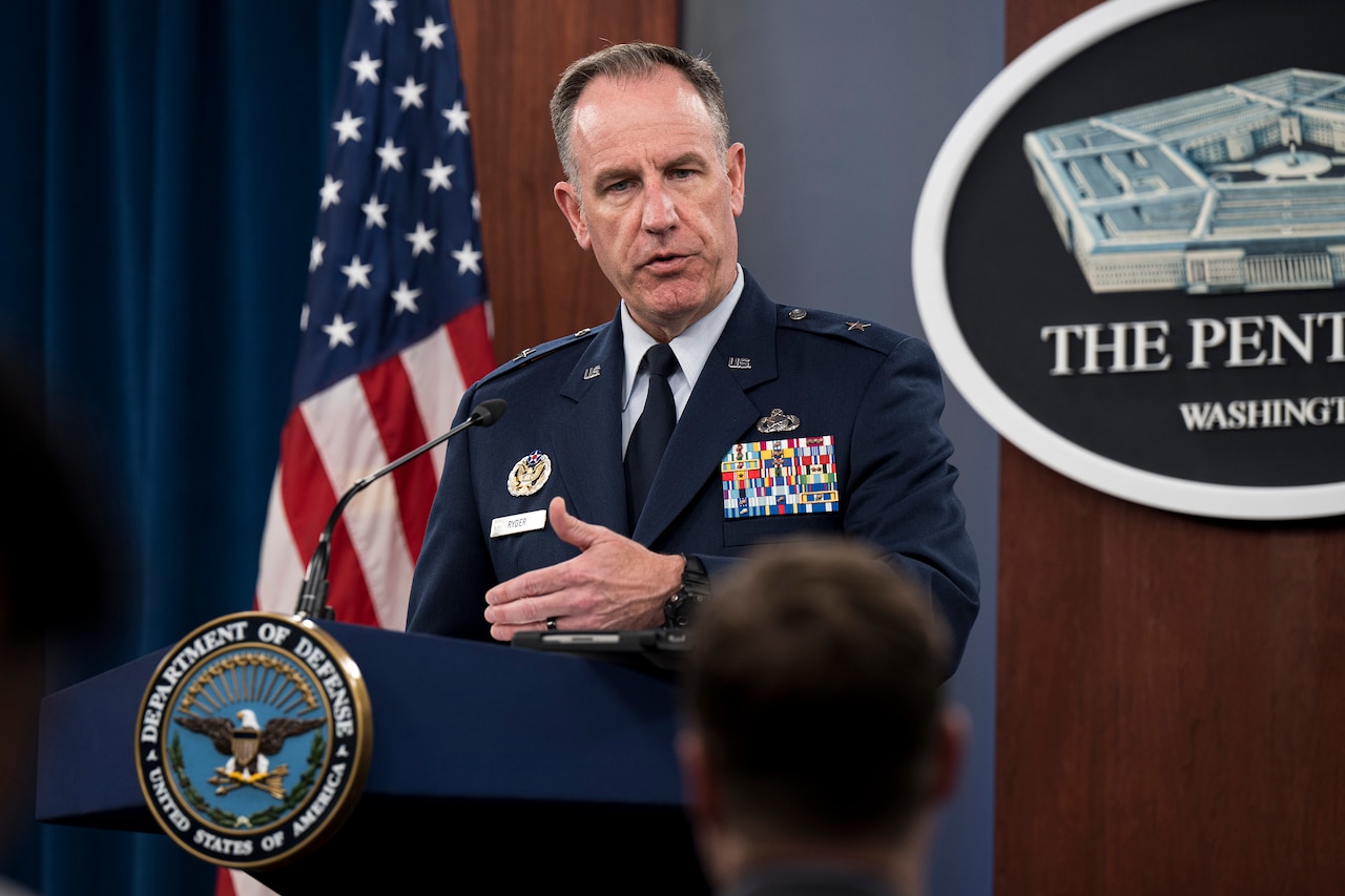 An Air Force general stands at a lectern and speaks to a seated audience.