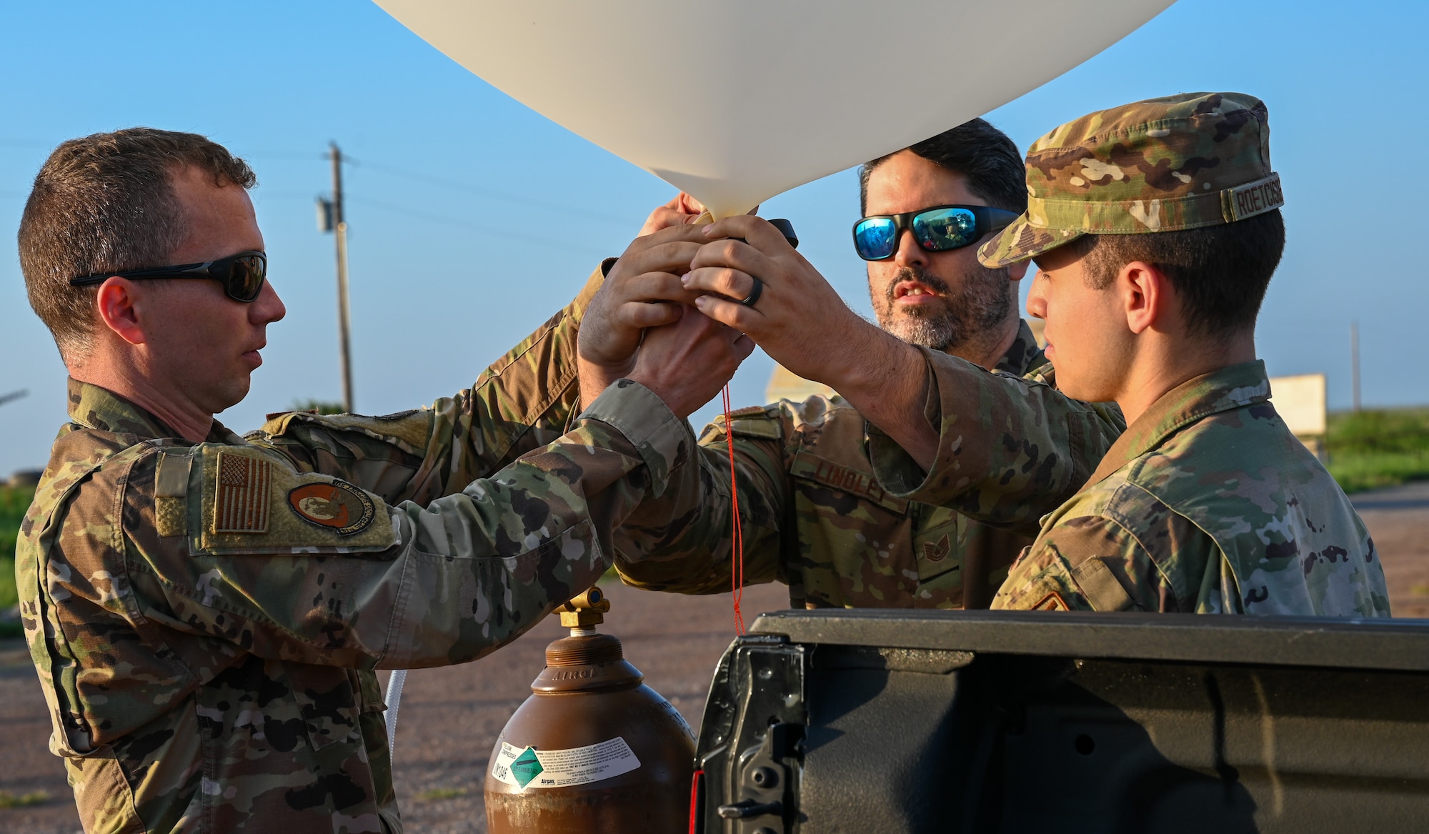 From the left, U.S. Air Force Capt. Ryan Tharp, 97th Operations Support Squadron (OSS)weather flight commander, Tech. Sgt. Jared Lindley, 97th OSS noncommissioned officer in charge of weather operations, and Airman 1st Class Cameron Roetcisoender, 97th OSS weather apprentice, inflate a weather balloon at the Sooner Drop Zone, June 15,2023. The balloons launch up to 60,000 feet to capture data on the temperature dew point, pressure, wind speed, and wind direction using a radiosonde device. (U.S. Air Force photo by Airman 1st Class Heidi Bucins)