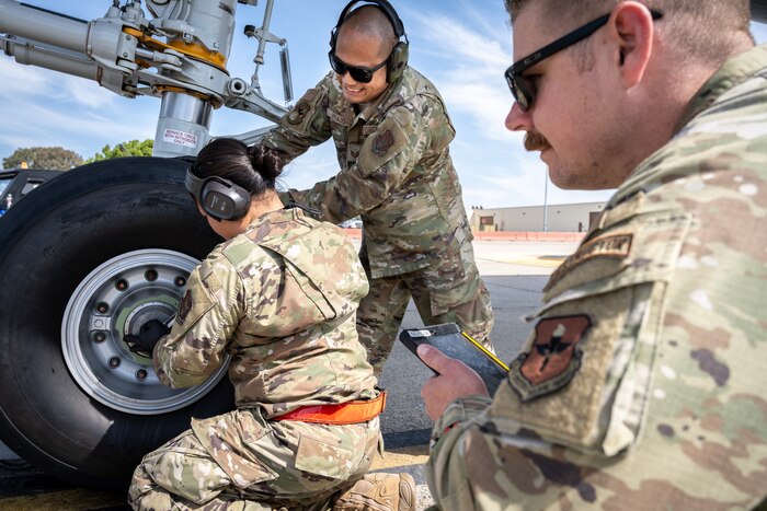 Three Airmen work on a tire change of an aircraft