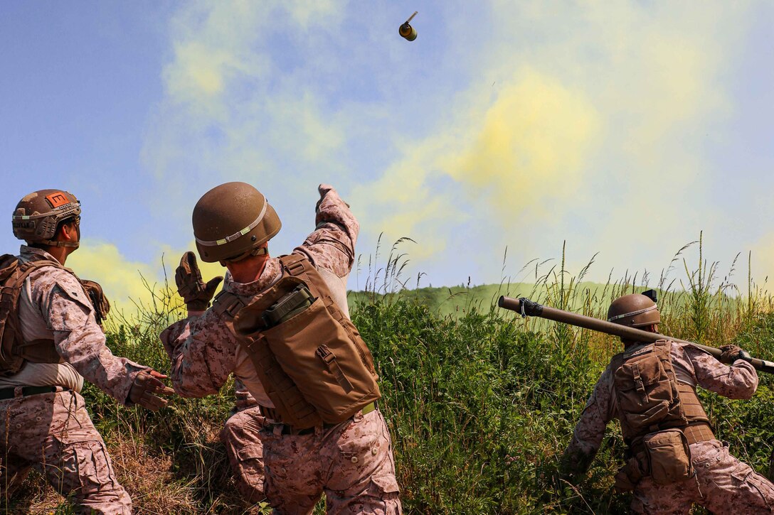 A Marine throws a smoke grenade during an explosive breaching training while others look on.