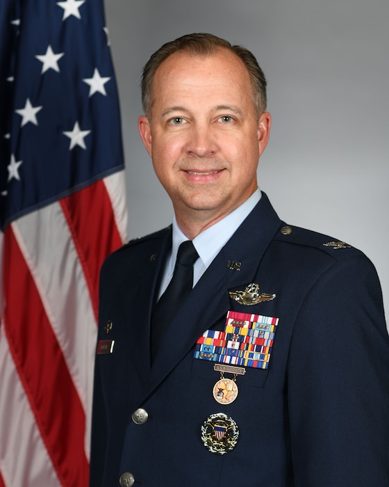 Man in a blue uniform poses in front of an American flag.