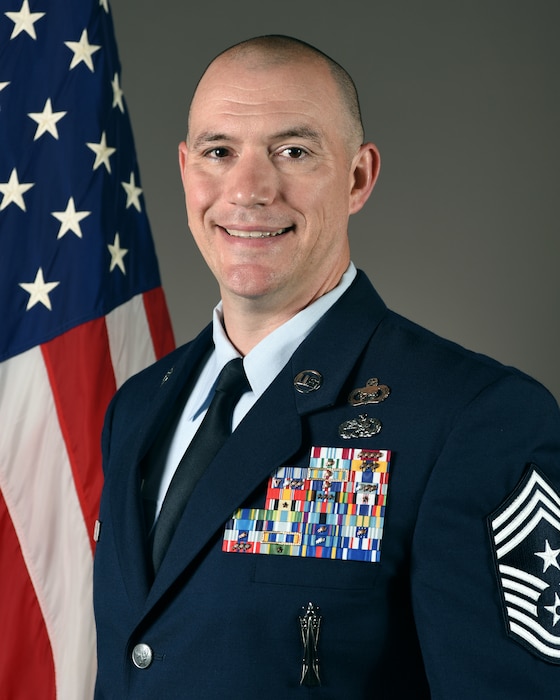 Man in blue uniform poses in front of American flag.