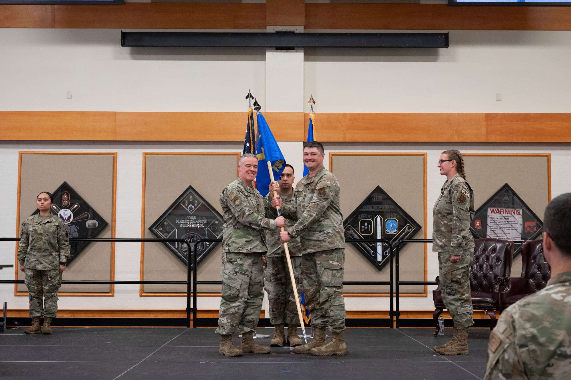 Three military personnel in uniform conduct the passing of a squadron flag to represent the official changing of command.