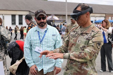 Solder in fatigues wears a virtual reality goggle while a trainer looks on to guide his experience and explain the technology.
