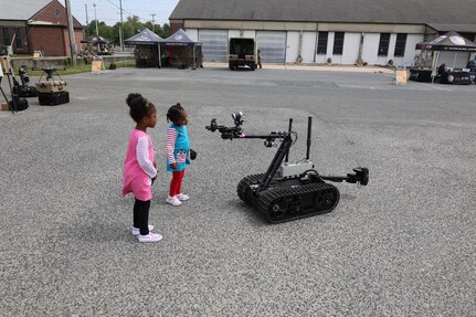 two little girls stand in a parking lot in front of the semi-autonomous robot