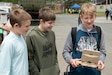 Three boys stand and one holds a controller for a semi-autonomous vehicle.