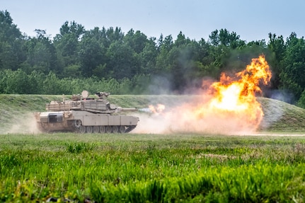 Tank rolls through a test fire range and a smoke and fire cloud bare in the foreground.