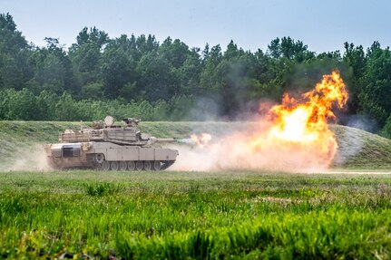 Tank rolls through a test fire range and a smoke and fire cloud bare in the foreground.