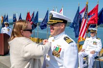 Cmdr. Todd Galvin, commander NAVMAG Indian Island, is pinned with a command ashore pin by his wife during a change of command ceremony that took place on the ammunition pier in Port Hadlock, Washington, June 22, 2023. During the ceremony, Cmdr. Andrew Crouse was relieved as commander of NAVMAG Indian Island while Cmdr. Todd Galvin assumed his position as the incoming commanding officer. (U.S. Navy photo by Mass Communication Specialist 2nd Class Gwendelyn L. Ohrazda)