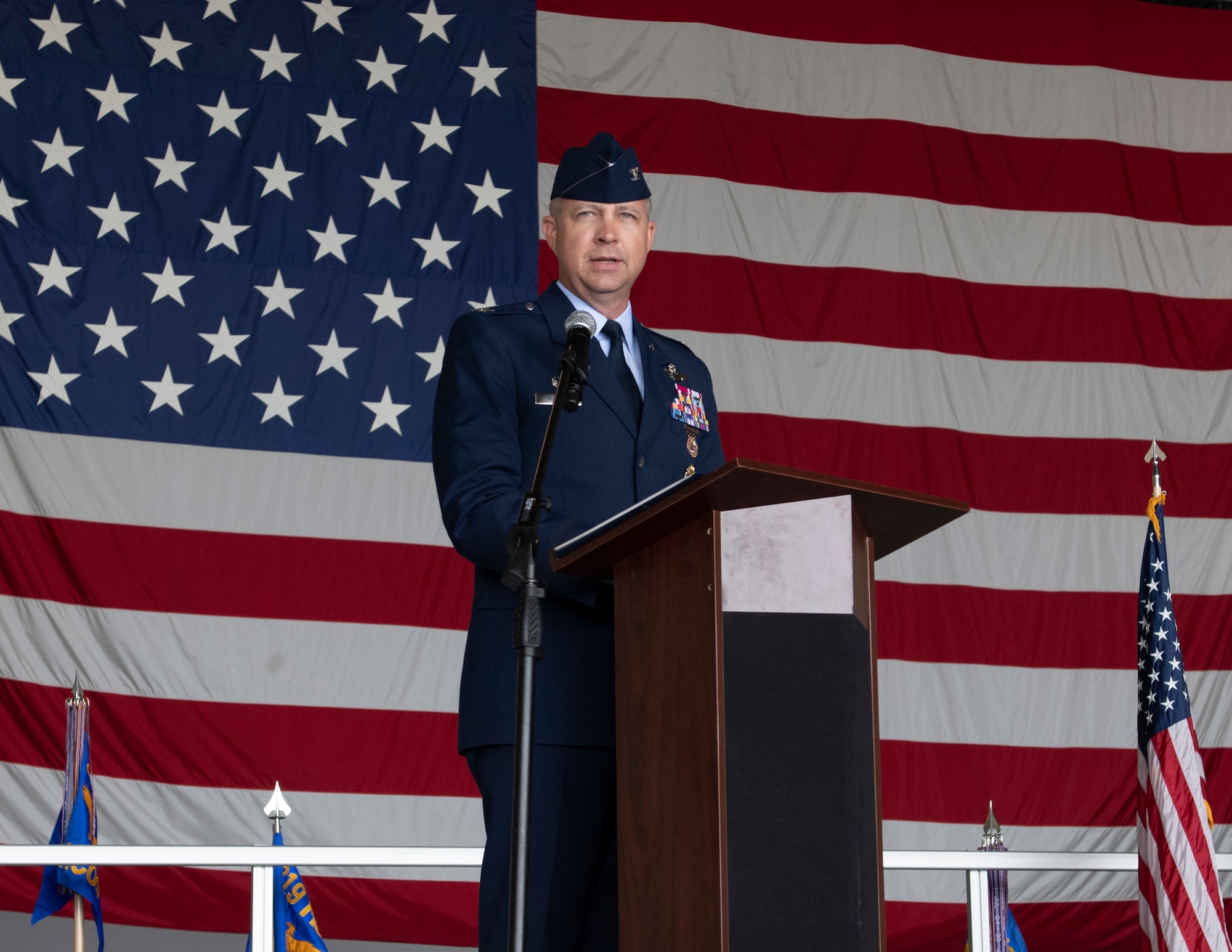 A man in a blue suit speaks at a podium in front of an American flag.