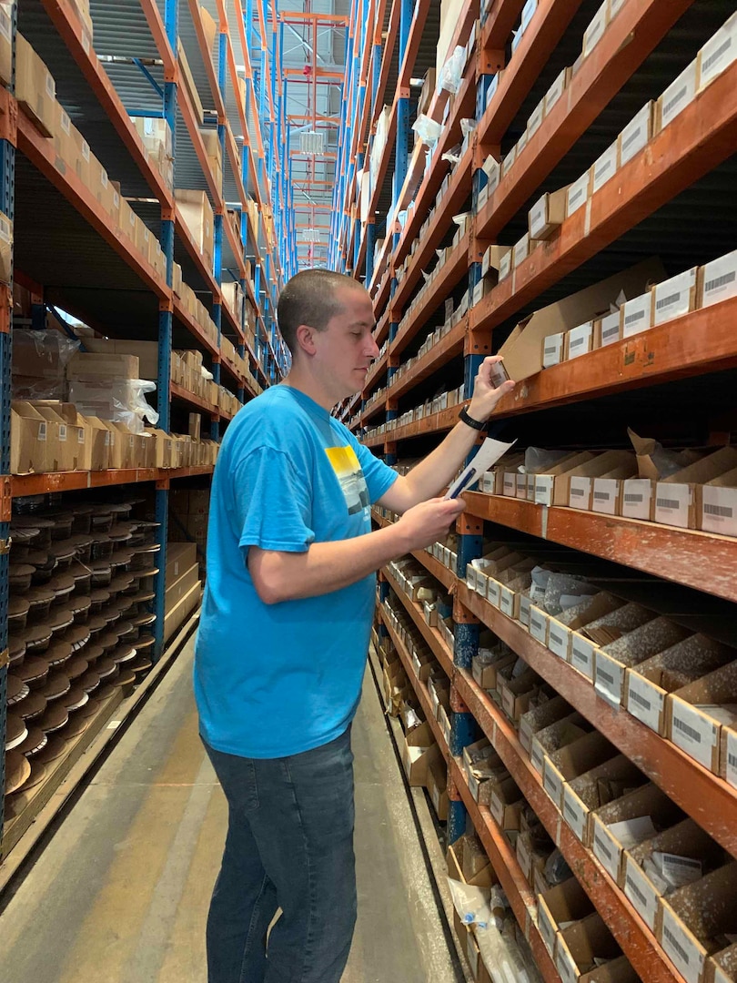 Jacob West stands in warehouse picking an item from a bin.
