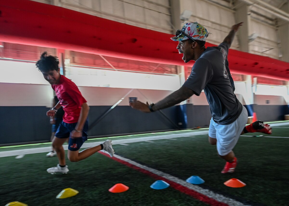 A photo of a man chasing a child during a football drill.