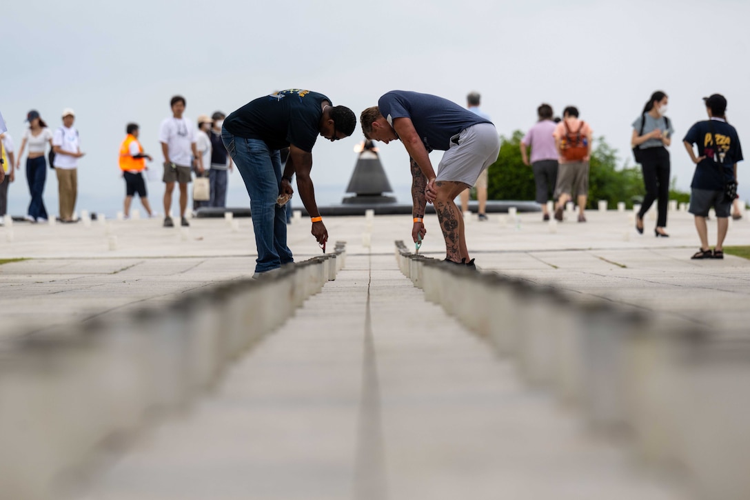 Two sailors light a long row of candles.