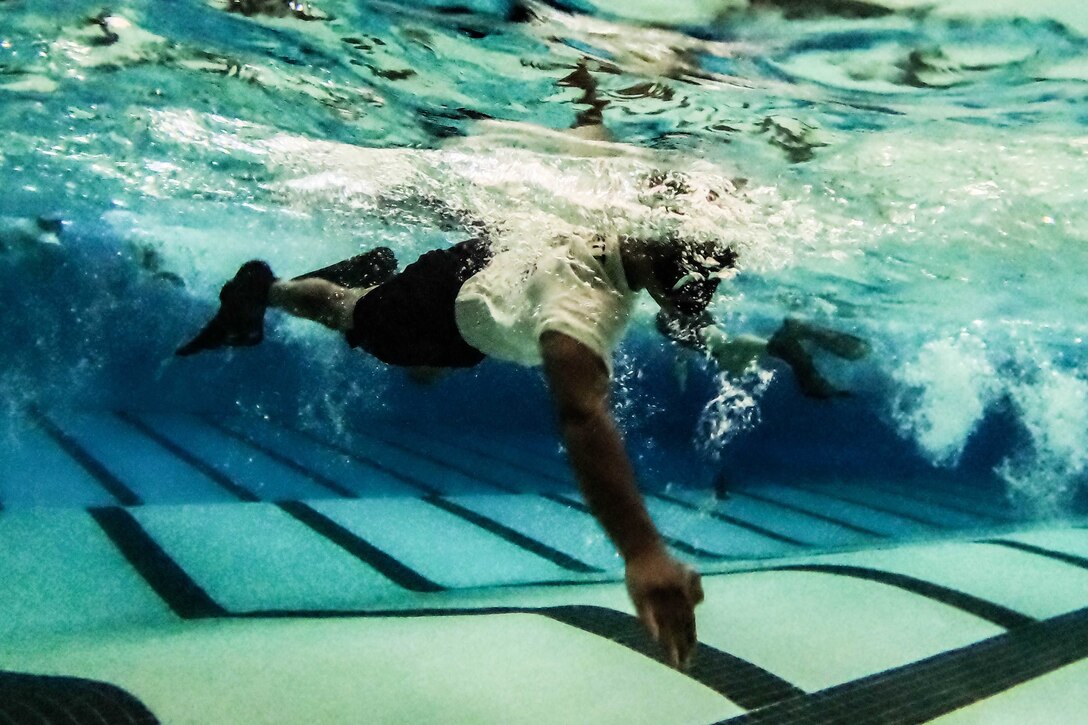 A sailor swims mostly underwater in a pool.