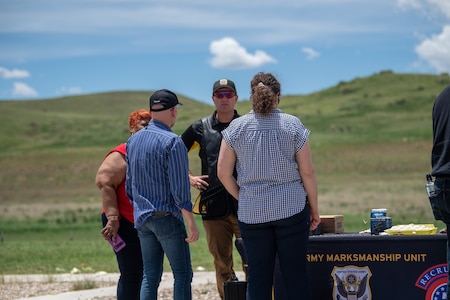 Group of people stand around Army Marksmanship Unit demonstration table.